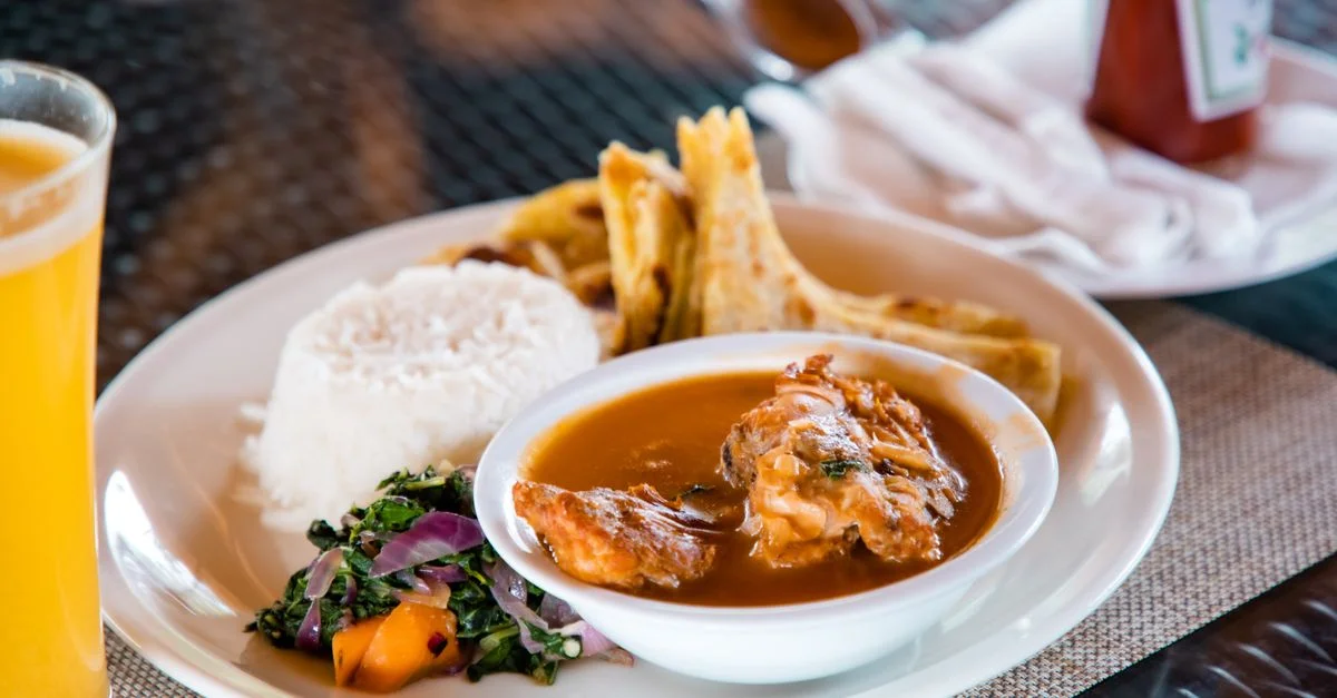 Délicieux plat traditionnel ougandais avec du riz, un ragoût, des légumes verts et un chapati sur une table à manger.