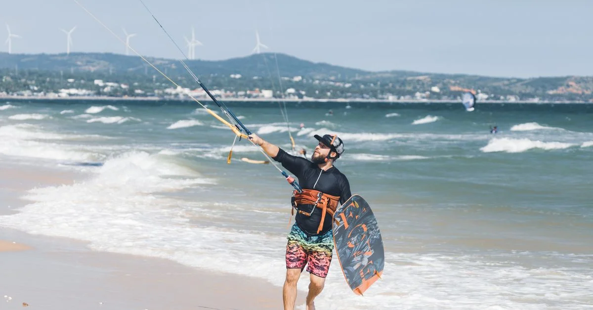 Homme kitesurfant sur une plage ensoleillée, profitant de l'aventure sous un ciel dégagé.