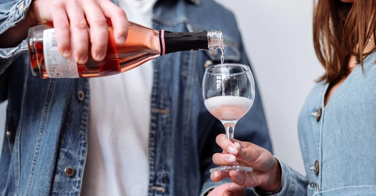 Un couple en tenues en denim versant du vin rosé dans un verre, suggérant une célébration.